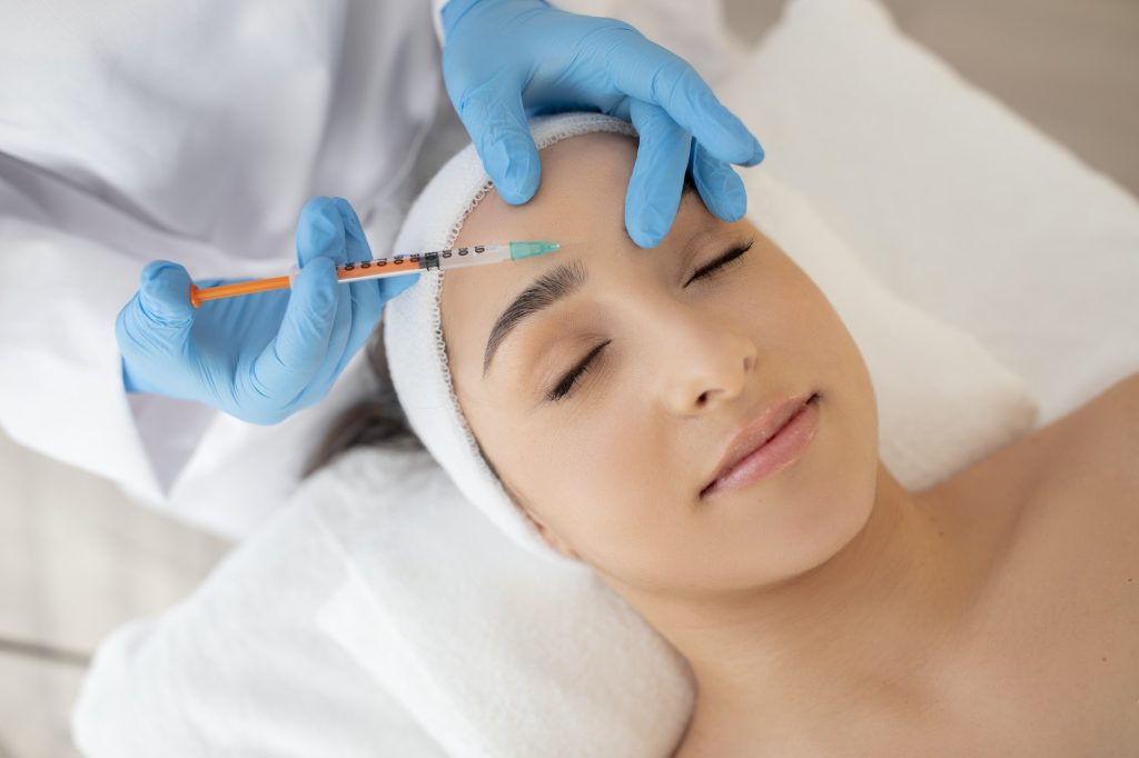 Aesthetic Treatment. Young beautiful woman getting injection on forehead in salon, closeup